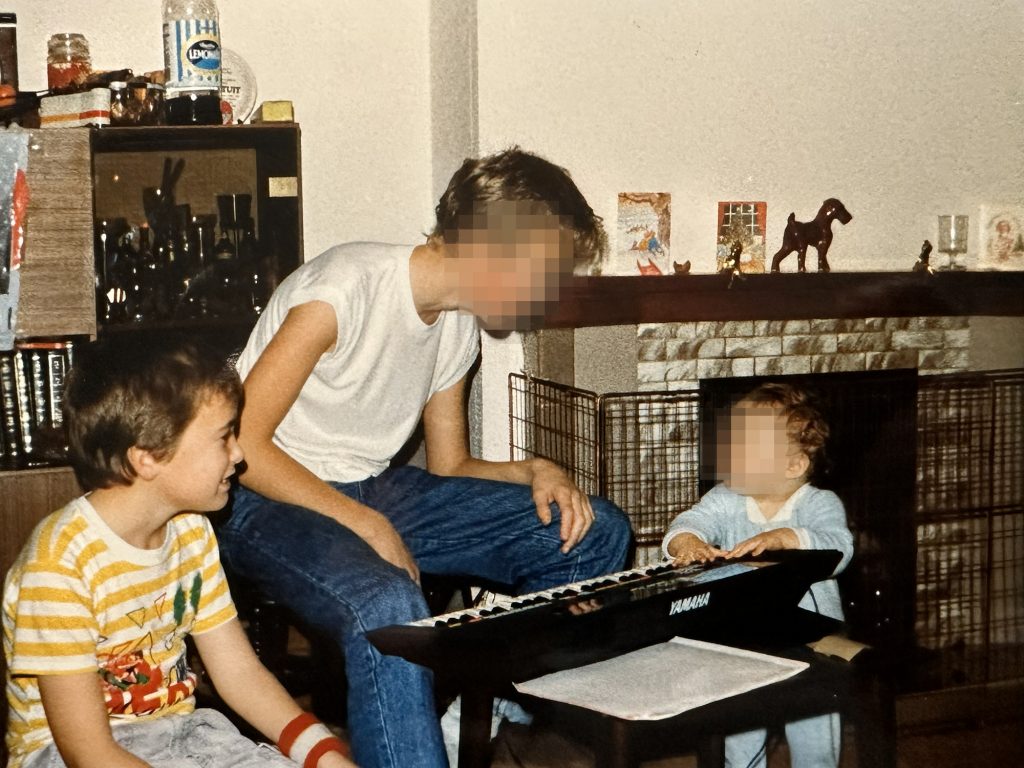 1980s photograph of a family living room in Essex, with a brick fireplace visible in the background and children playing in the foreground