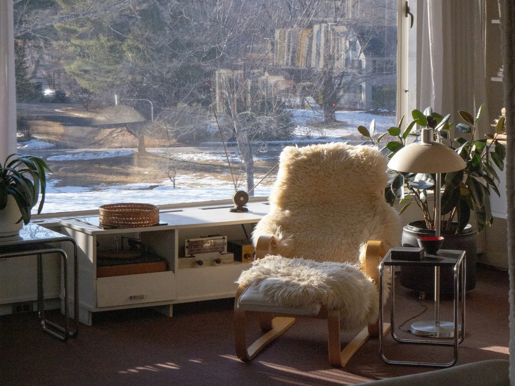 Scandinavian-style living room with large windows overlooking a snowy winter garden, featuring a sheepskin-draped chair bathed in sunlight. Photo by Jerry Zheng on Unsplash