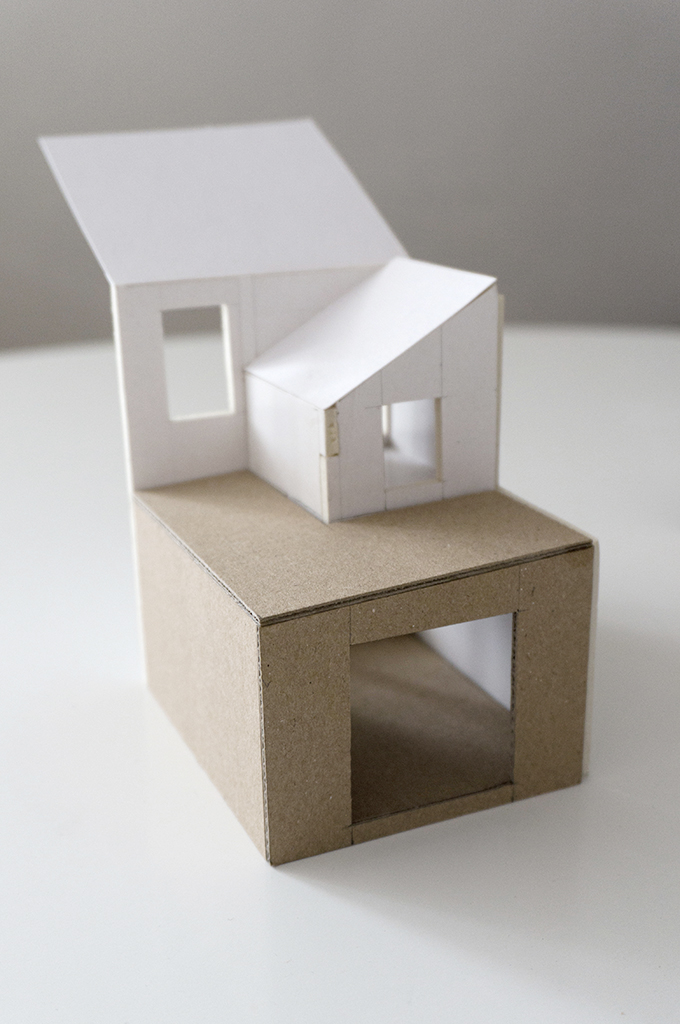 A photograph of cardboard model, showing an existing house in white and a proposed extension in contrasting brown